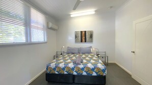 A bedroom with a bed, two bedside tables, a ceiling fan, a window with blinds, and a door.