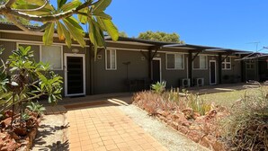 A motel with a paved walkway, air conditioning units, and a covered outdoor seating area.