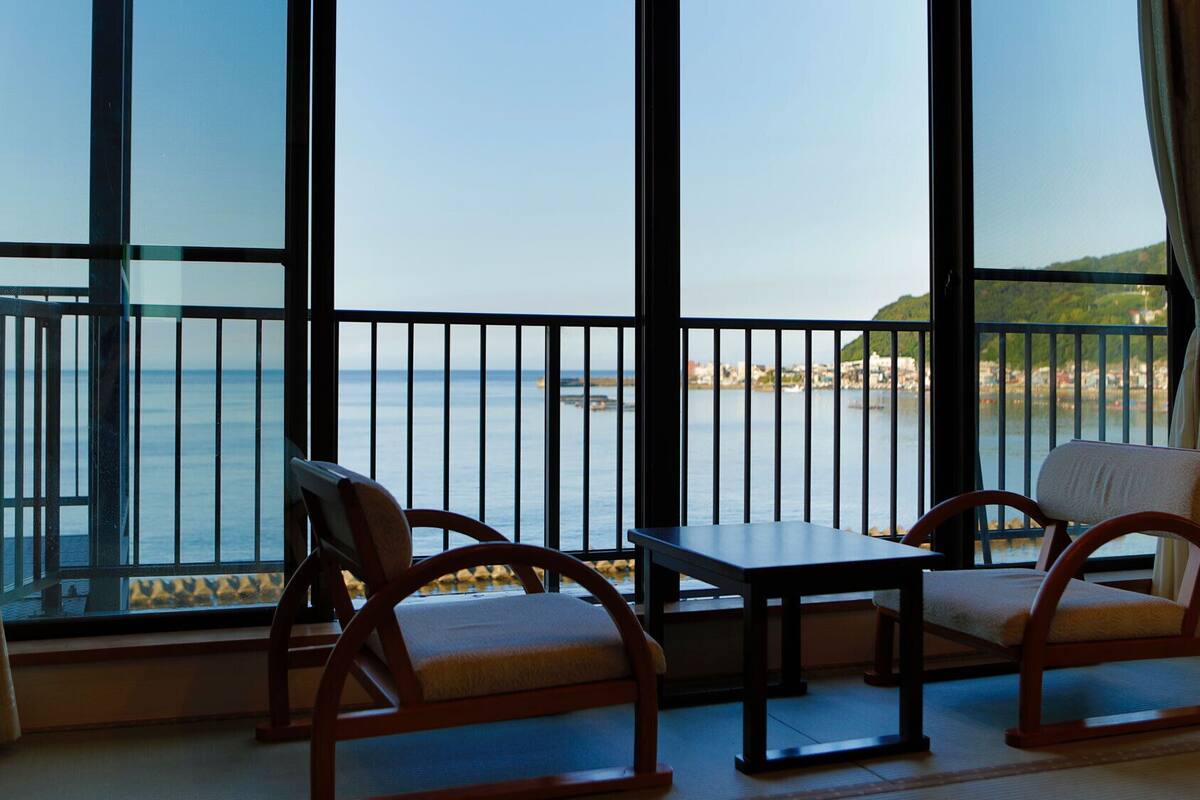 A balcony with a view of the sea, two wooden chairs, and a small table.