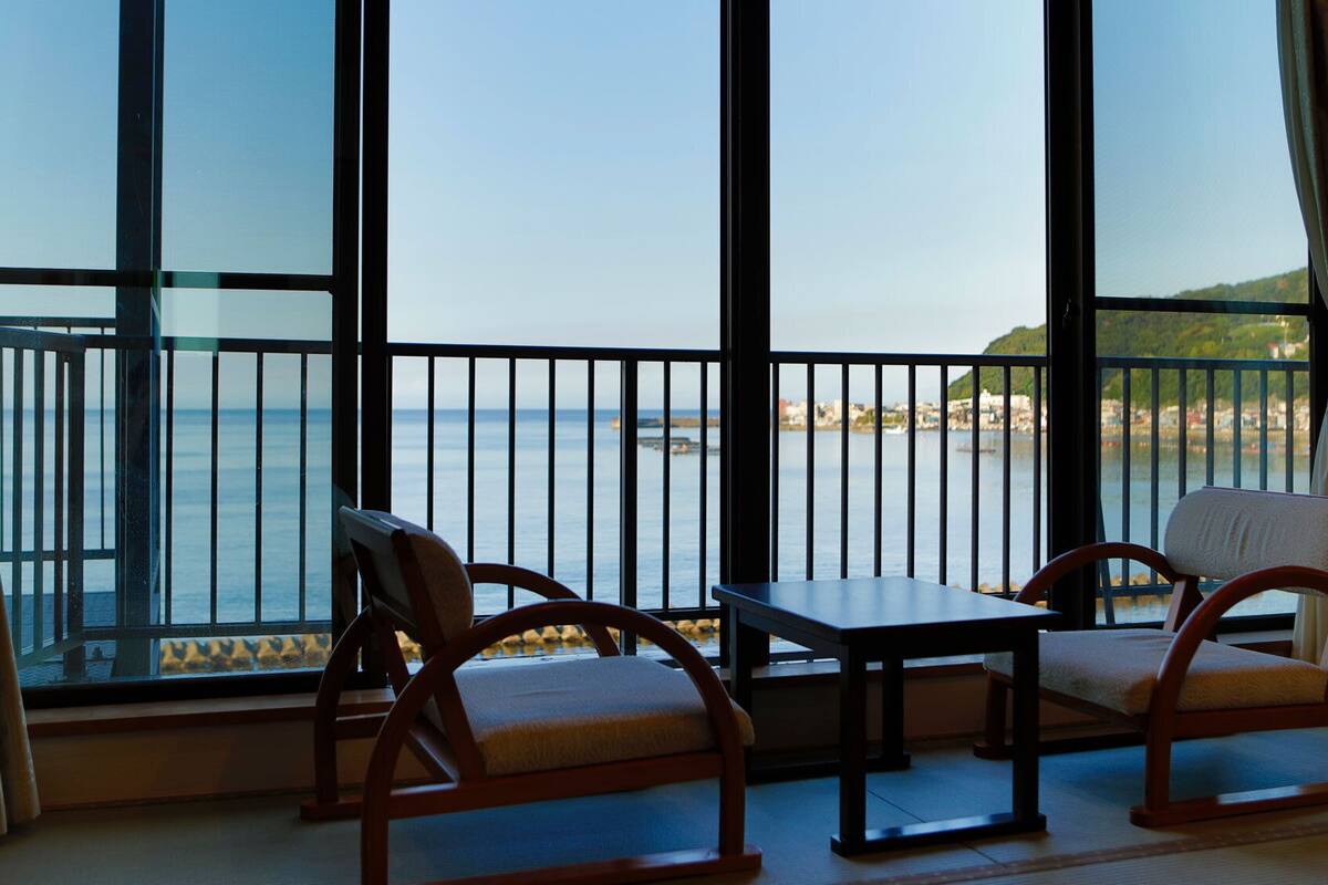 A room with a large window overlooking a body of water, two wooden chairs, and a small table.