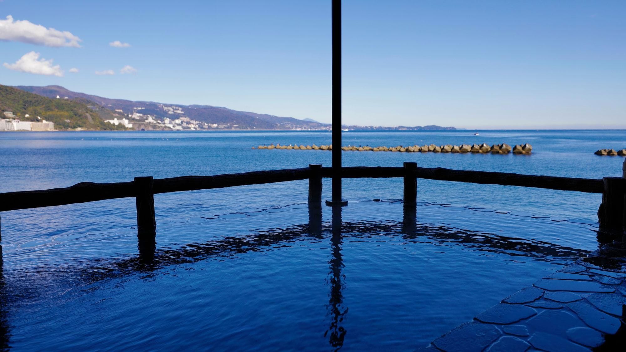 A waterfront view with a wooden fence, calm water, and distant buildings.