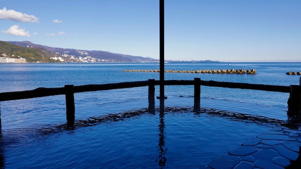 A waterfront view with a wooden fence, calm water, and distant buildings. - Atami Onsen Hiratsuru (Atami)