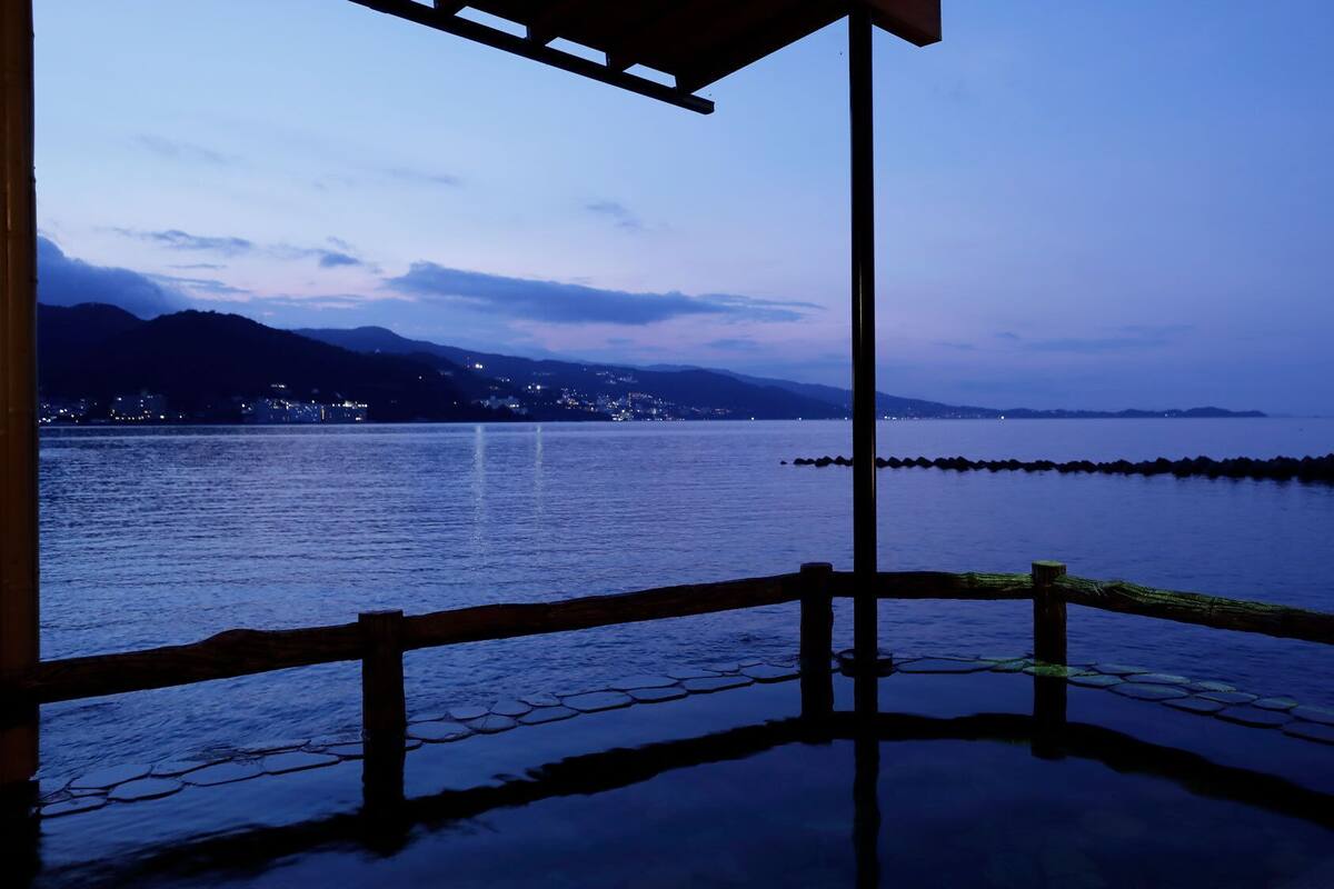A waterfront view with a wooden deck, a distant cityscape, and mountains in the background.