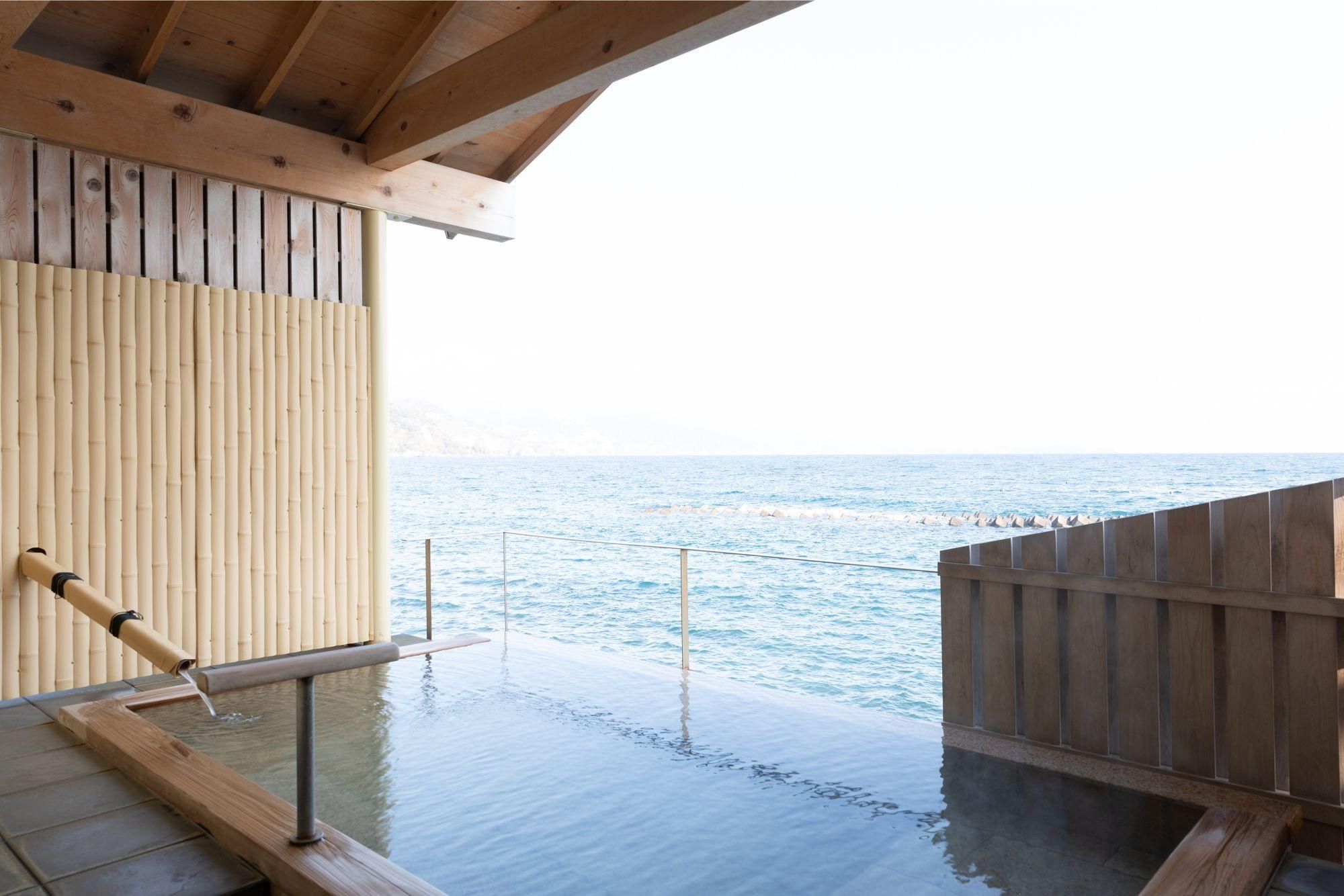 A wooden deck with a view of the sea, a bamboo screen, and a wooden railing.