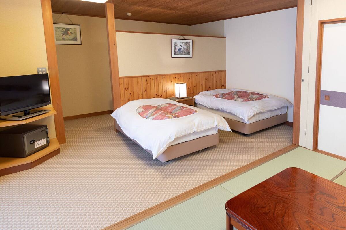 A hotel room with two beds, a TV, a safe, a wooden table, and a futon.