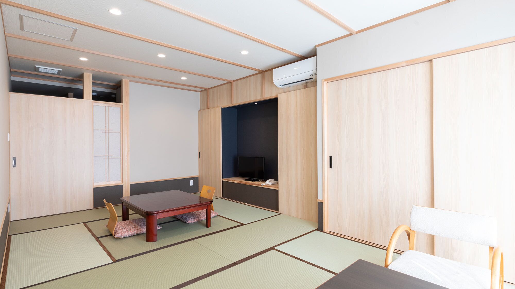 Una habitación tradicional japonesa con suelo de tatami, una mesa de madera baja, un televisor y puertas correderas.