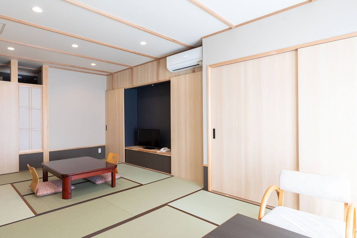 A traditional Japanese-style room with tatami flooring, a low wooden table, a television, and sliding doors.