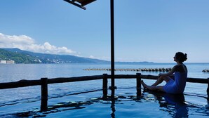A person sitting by a waterfront, overlooking a calm sea with a distant shoreline. - Atami Onsen Hiratsuru (Atami)
