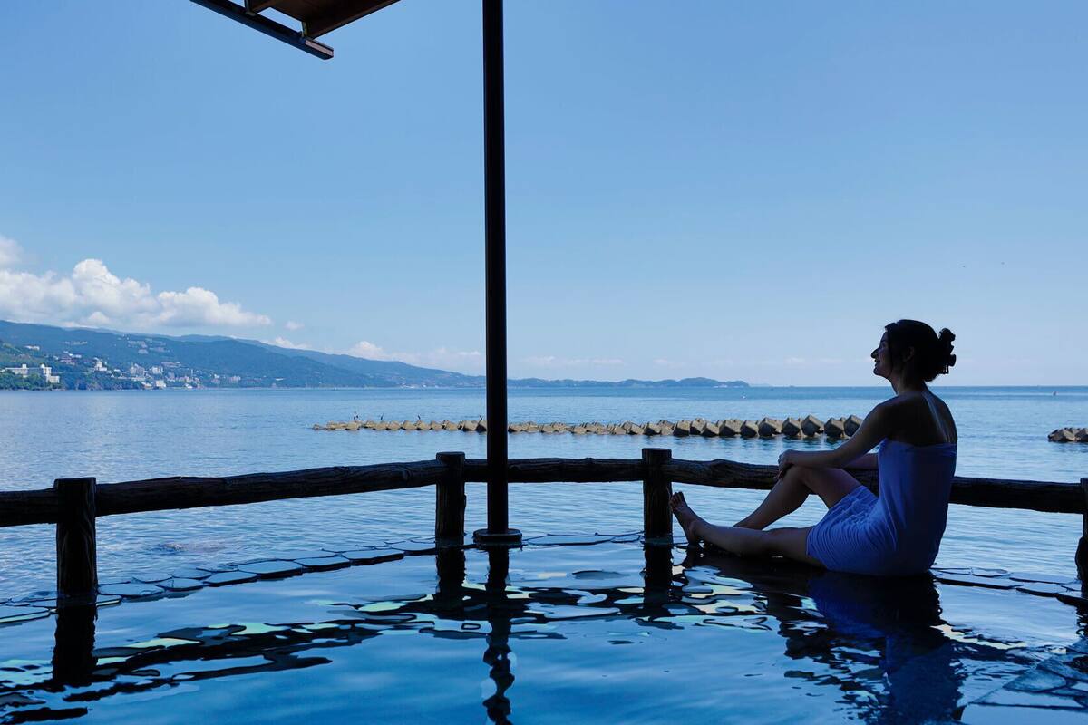 A person sitting by a waterfront, overlooking a calm sea with a distant shoreline.