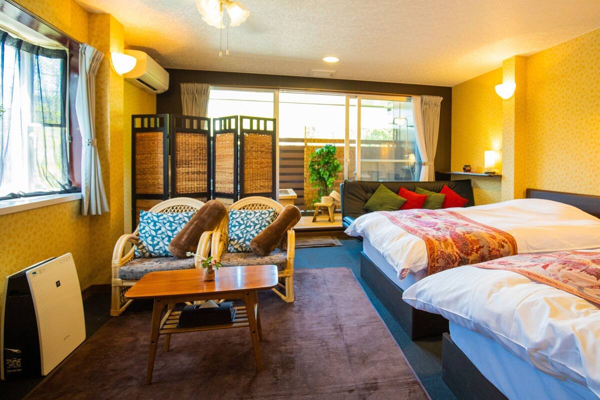 Una camera d'albergo con un divano, due letti, un tavolo e una finestra con tende.