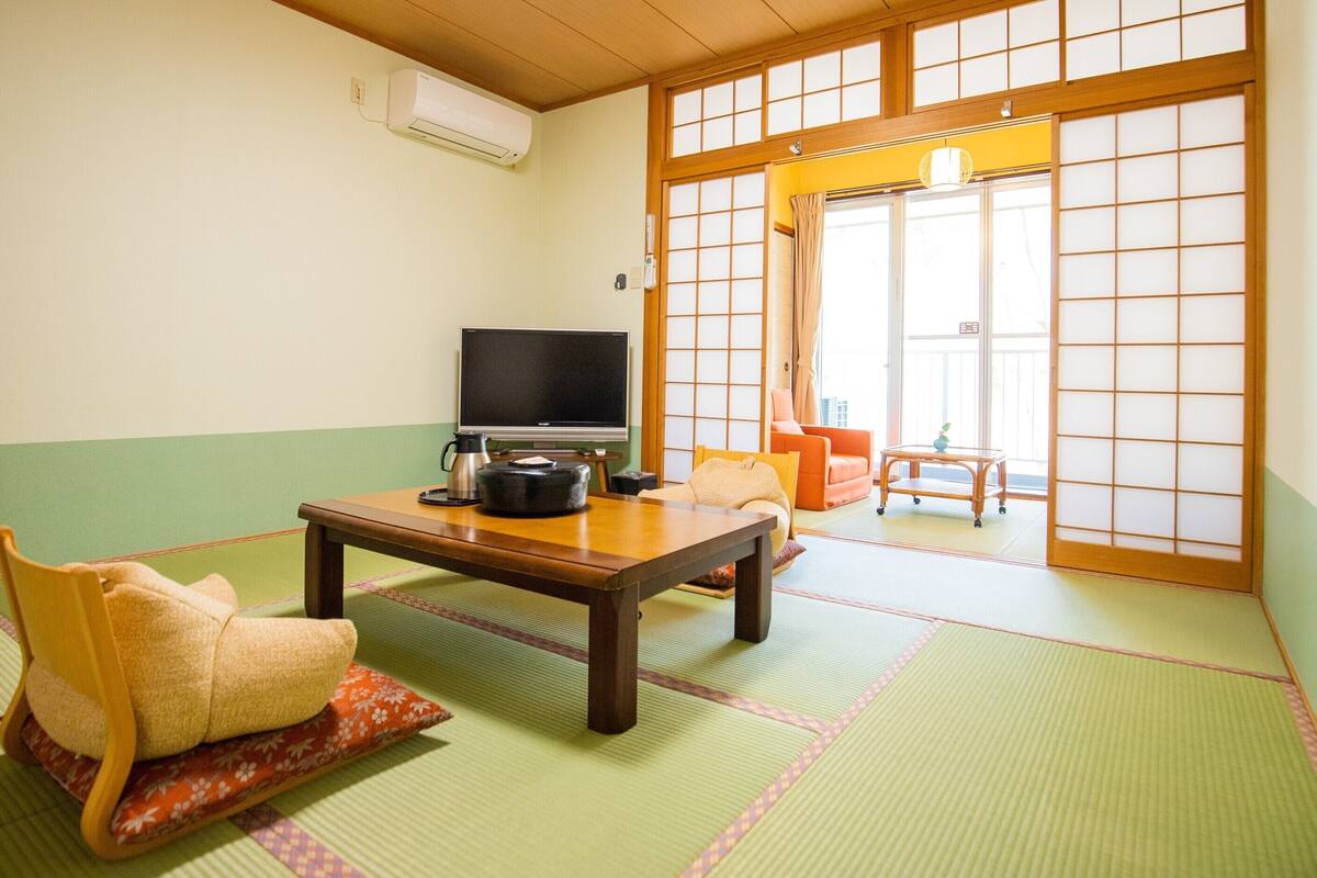 Una stanza tradizionale giapponese con pavimento in tatami, una televisione, un tavolo con un bollitore e un divano.