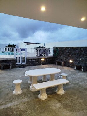 An outdoor patio with a stone wall, a pool area with a closed gate, and a table with benches. - Pôr do Sol is an accommodation located in R.Grande,close to Santa Barbara beach  (Ribeira Grande)