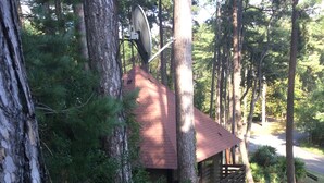 Een chalet met een rood dak, omringd door bomen, een schotelantenne en een houten terras.