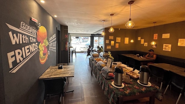 A restaurant interior with a long counter, tables, and a wall with a motivational quote. - Hotel Xenios (Macapa)