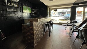 A bar area with a counter, stools, and a shelf with bottles. - Hotel Xenios (Macapa)