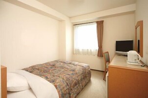 Una habitación de hotel con una cama, un escritorio con televisor y una ventana con cortinas.