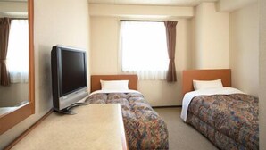 Una habitación de hotel con dos camas, televisión y ventana con cortinas.