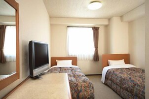 Una habitación de hotel con dos camas, televisión y ventana con cortinas.