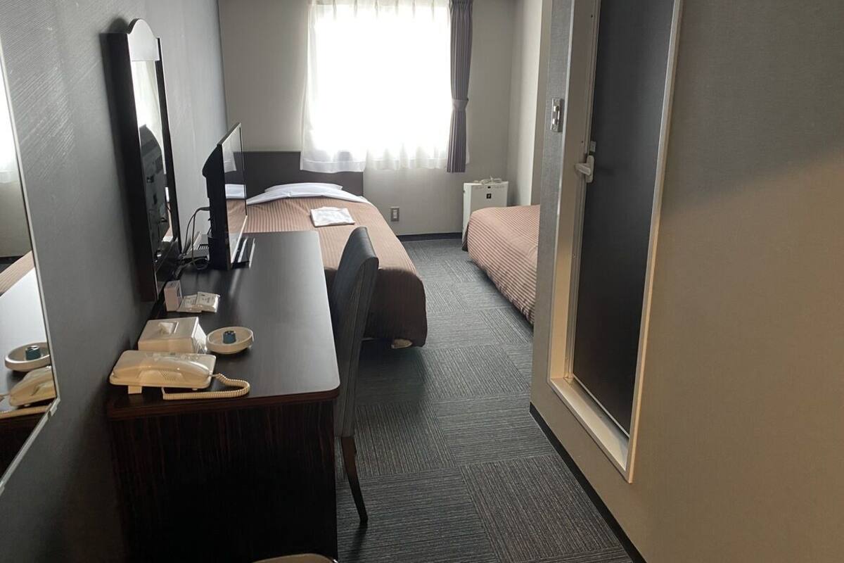 A hotel room with a desk, a bed, a mirror, a telephone, and a window with curtains.