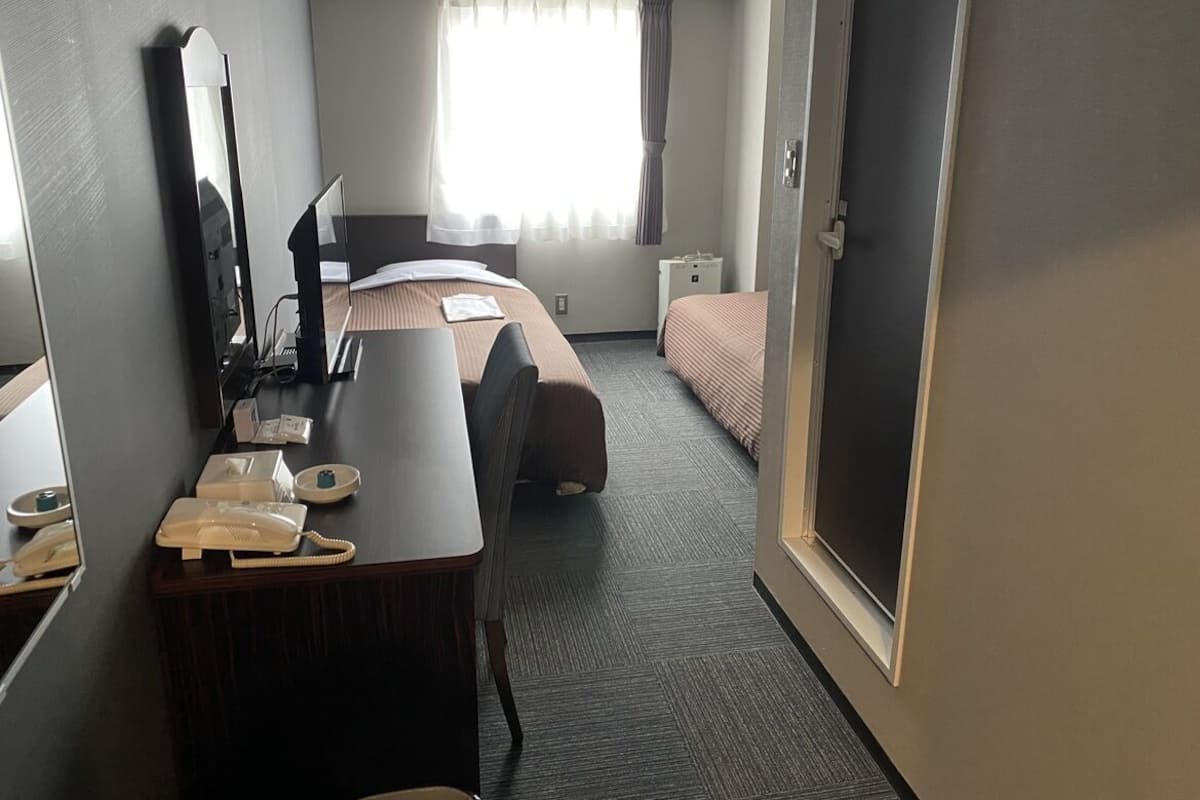 A hotel room with a desk, a bed, a mirror, a telephone, and a window with curtains.