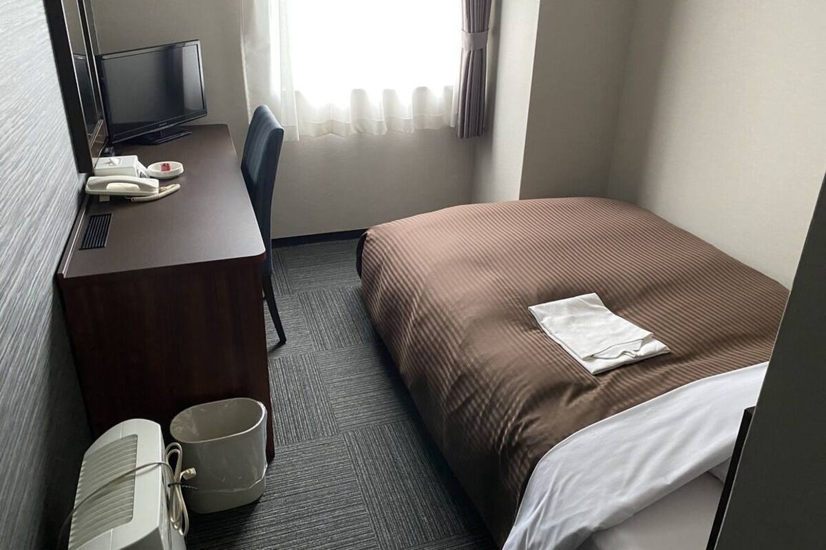 A hotel room with a bed, a desk with a telephone, a television, and a window with curtains.