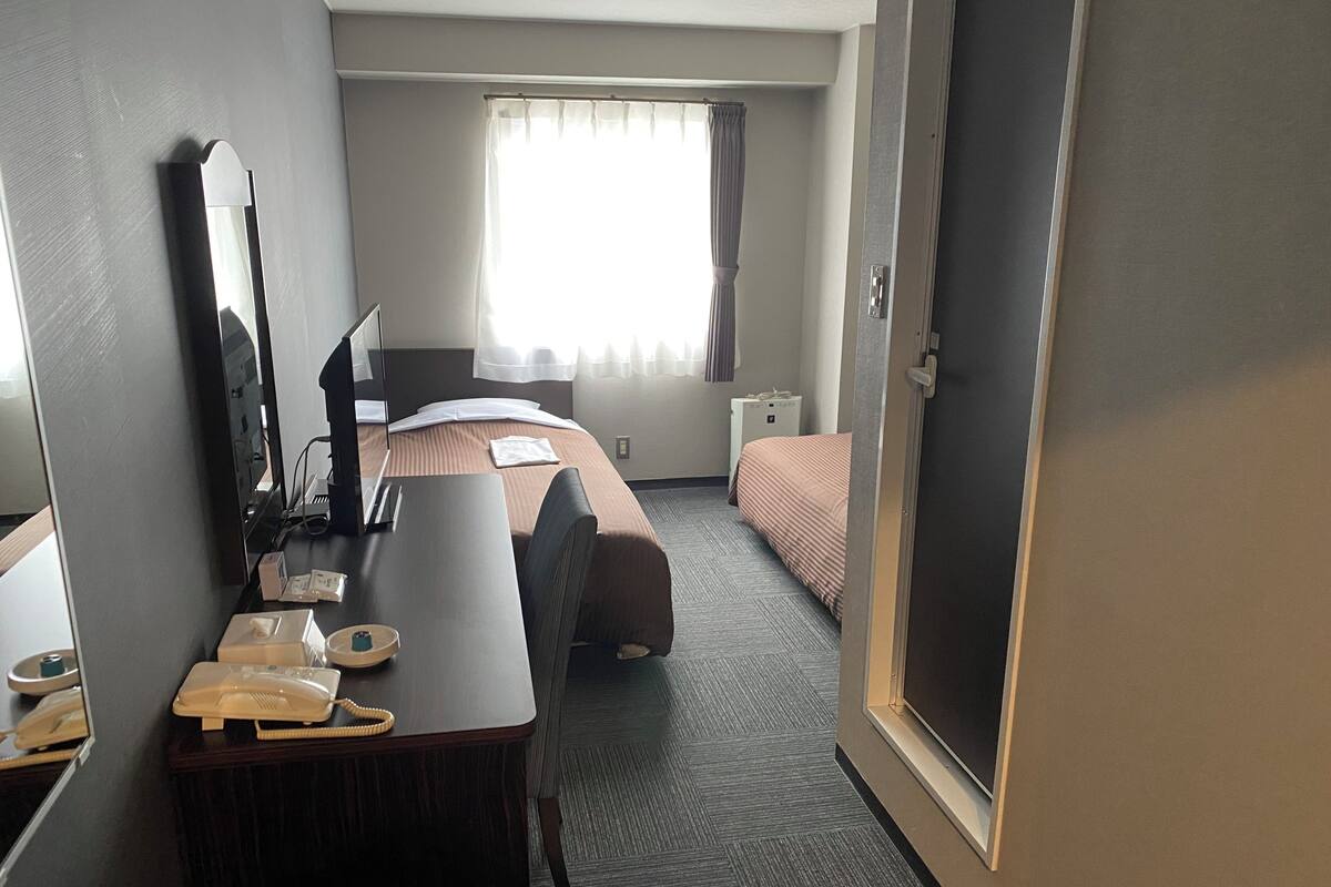 A hotel room with a bed, a desk with a telephone, a mirror, and a window with curtains.