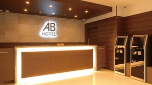 A hotel reception desk with a modern design, a sign above it, and two self-service kiosks. - Ab Hotel Isesaki (Isesaki)