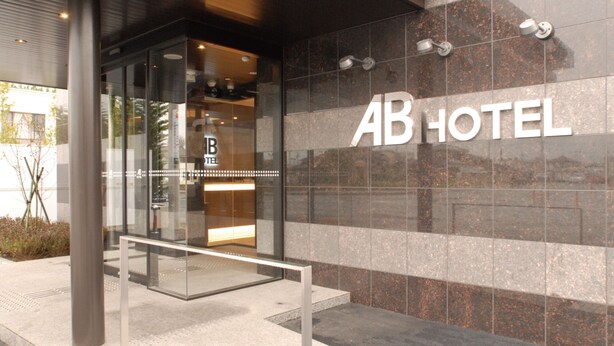 A hotel entrance with a glass door, a metal bench outside, and the name 'AB HOTEL' on the wall. - Ab Hotel Isesaki (Isesaki)