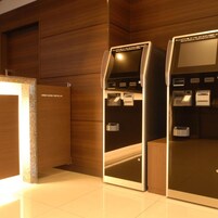 Un moderno vestíbulo de hotel con paneles de madera y dos quioscos de autoservicio para registro de entrada y salida.