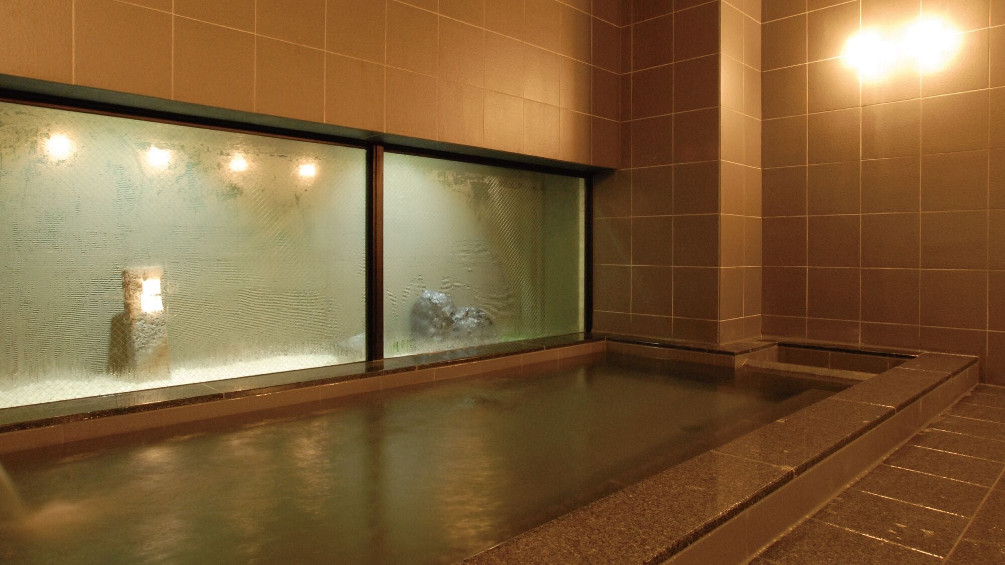 Un área de spa con pared de vidrio, bañera de hidromasaje y paredes con azulejos.