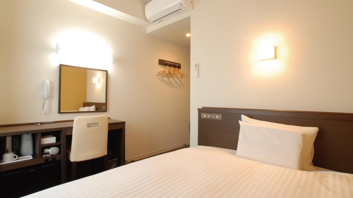 Habitación de hotel con cama, escritorio con teléfono, espejo y luz en la pared.