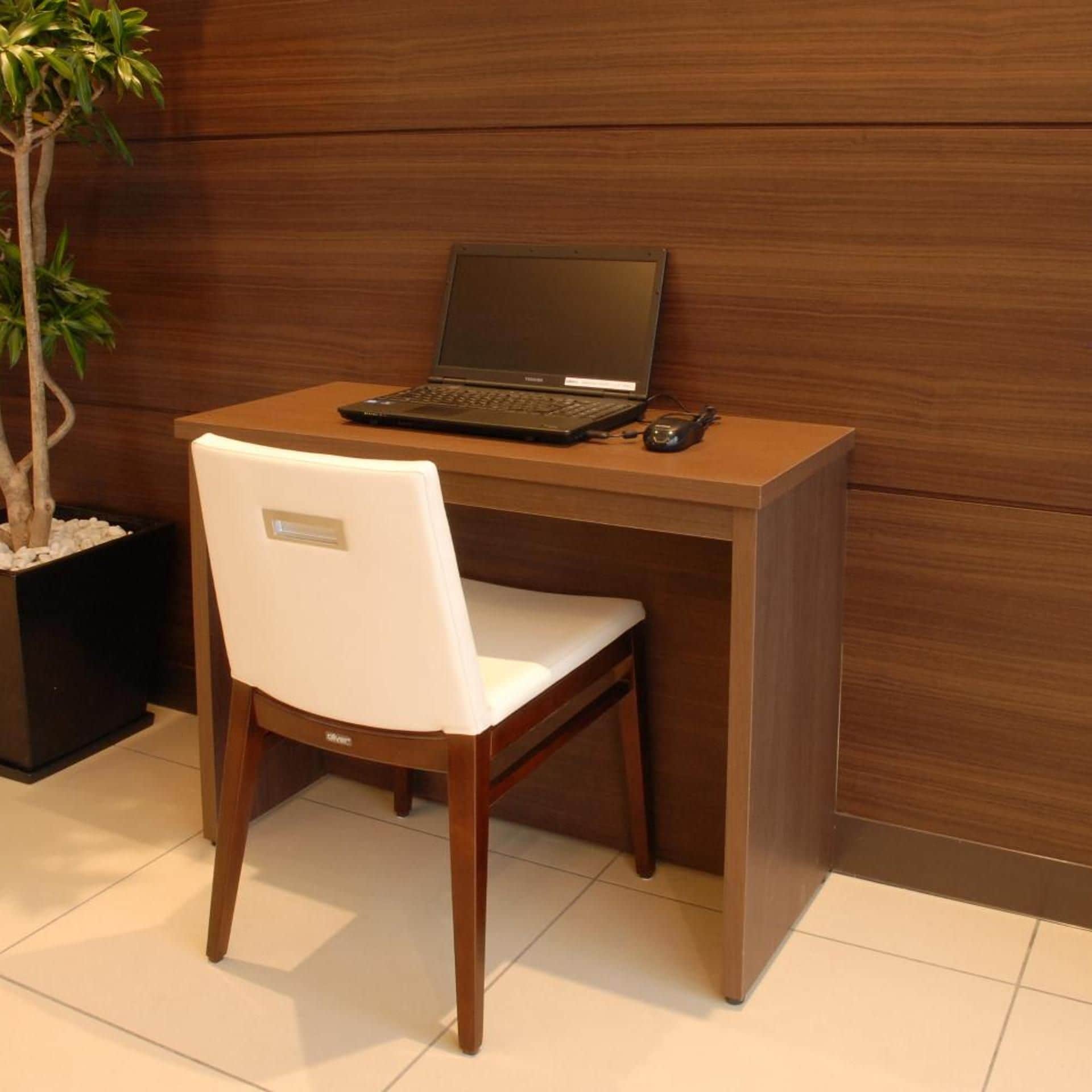 Een houten bureau met een laptop, een witte stoel en een potplant.
