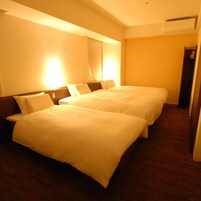 Habitación de hotel con dos camas, una mesita de noche y un equipo de aire acondicionado instalado en la pared.