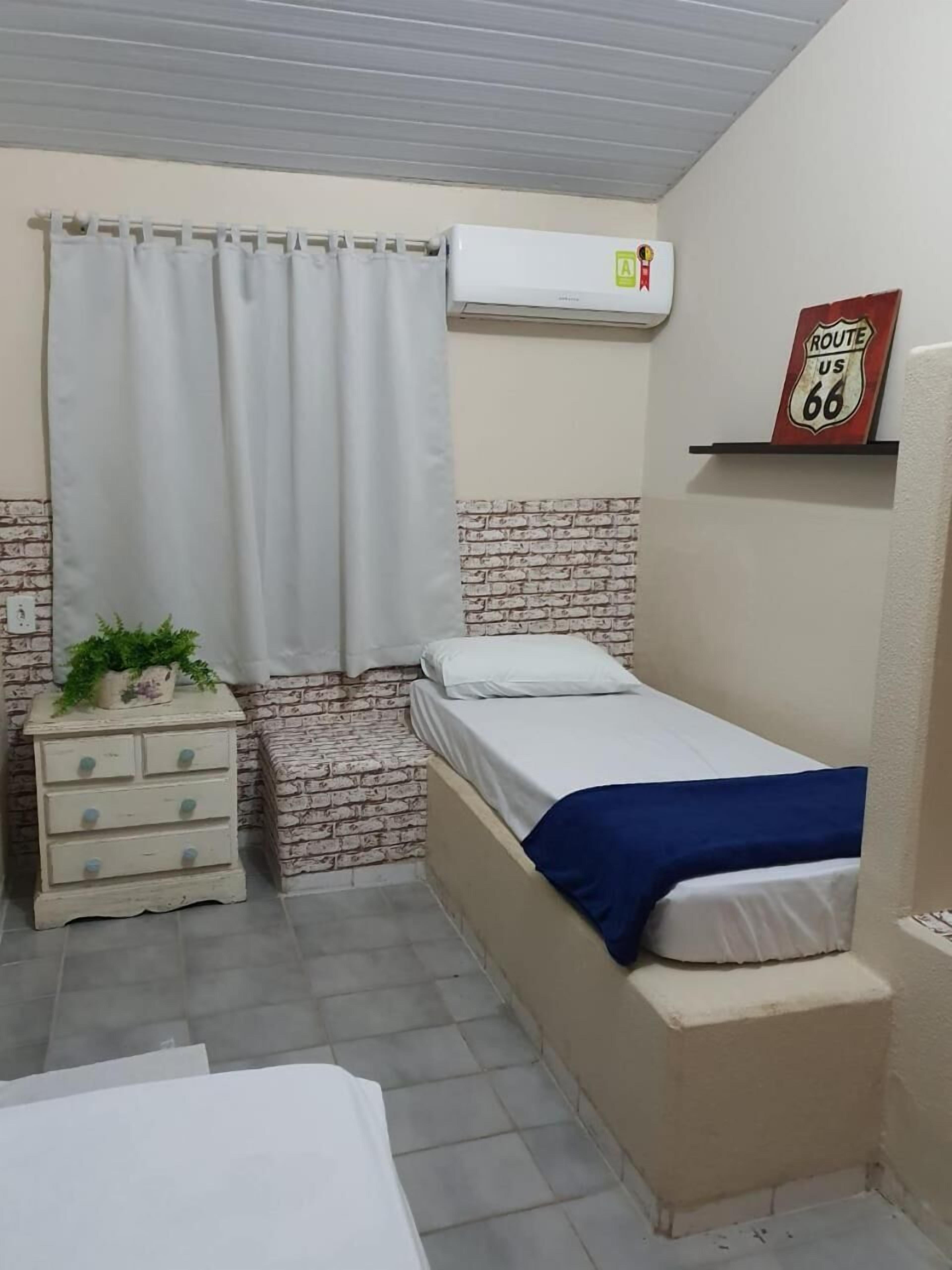 A small, compact room with a single bed, a dresser, and a wall-mounted air conditioner.