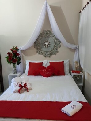 A neatly made bed with red and white bedding, a decorative wall piece, and a vase with flowers.