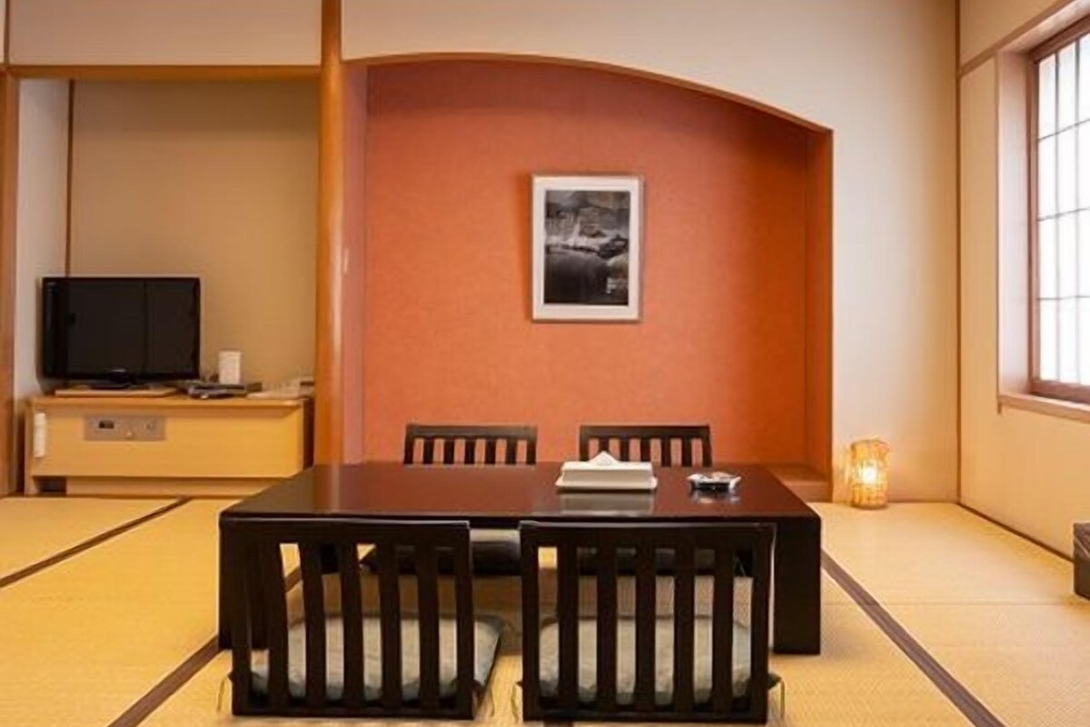 A traditional Japanese-style room with tatami flooring, a low table with cushions, a television on a cabinet, and a framed picture on the wall.