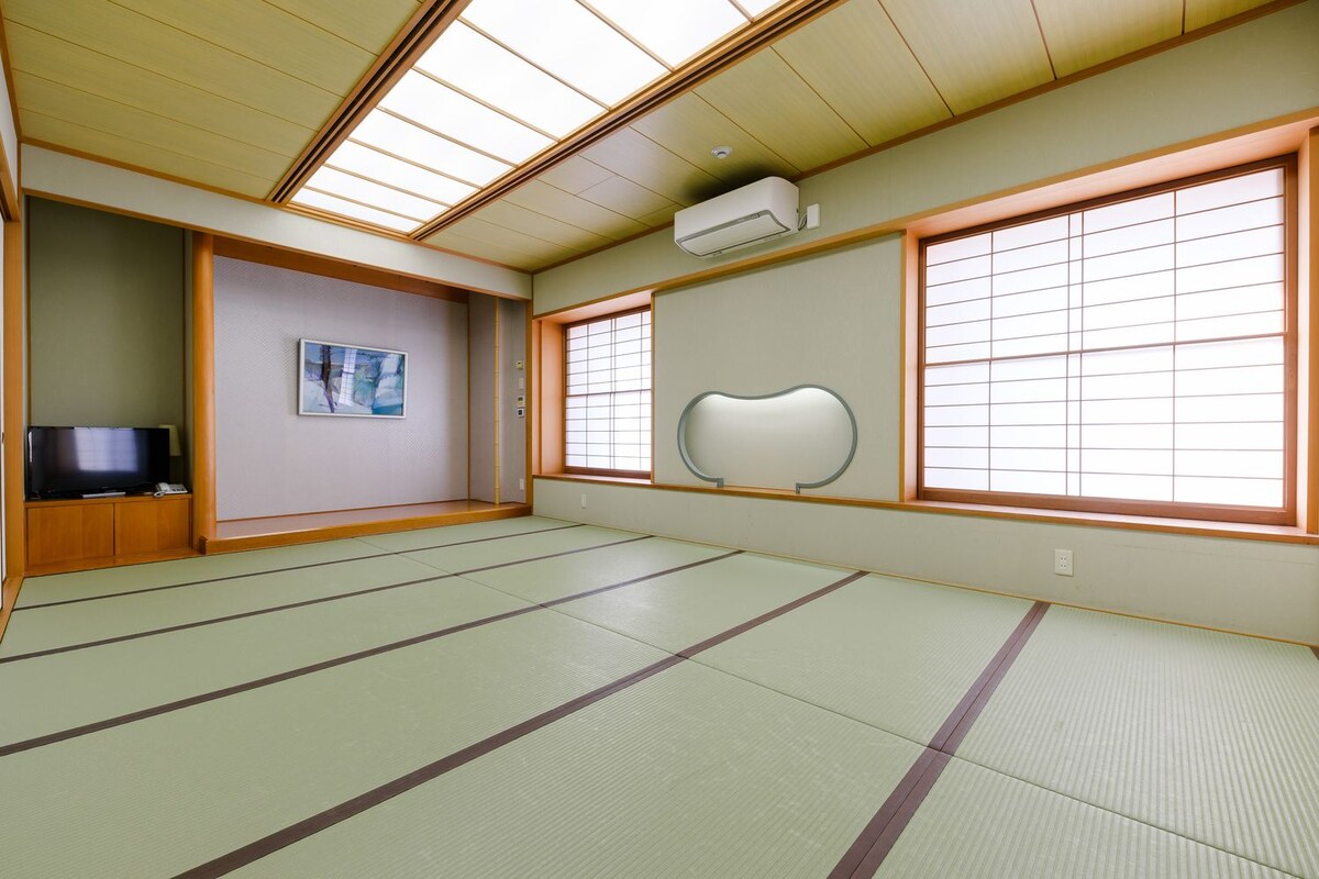 A tatami mat room with a television, a framed picture, and a large window with a decorative screen.