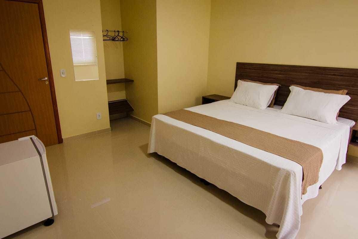 Une chambre d’hôtel avec un grand lit, une table de chevet, une petite commode, une porte en bois et un petit chariot.