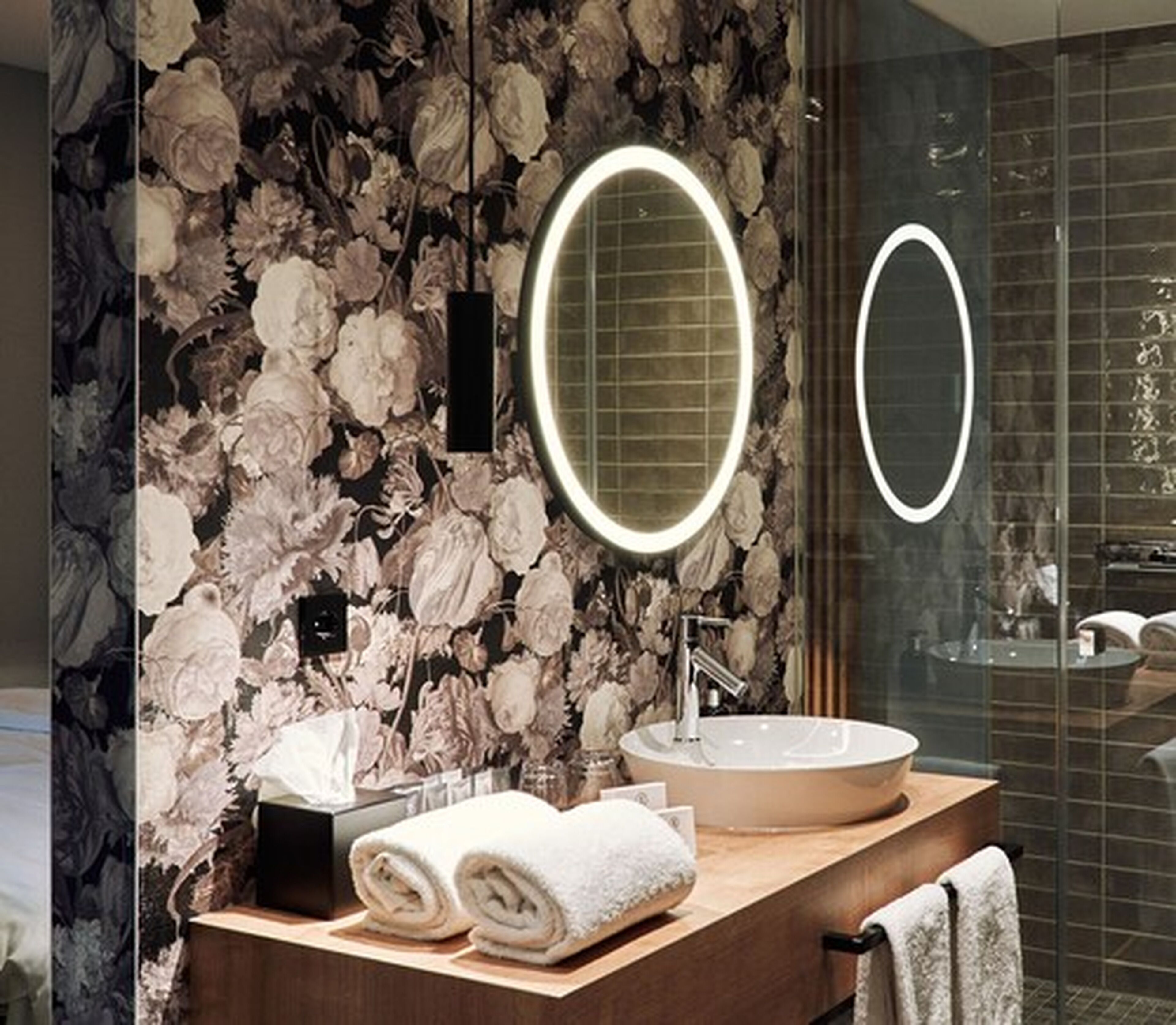 A bathroom with a marble wall, a round mirror, a sink, and towels.