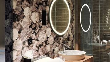 A bathroom with a marble wall, a round mirror, a sink, and towels.