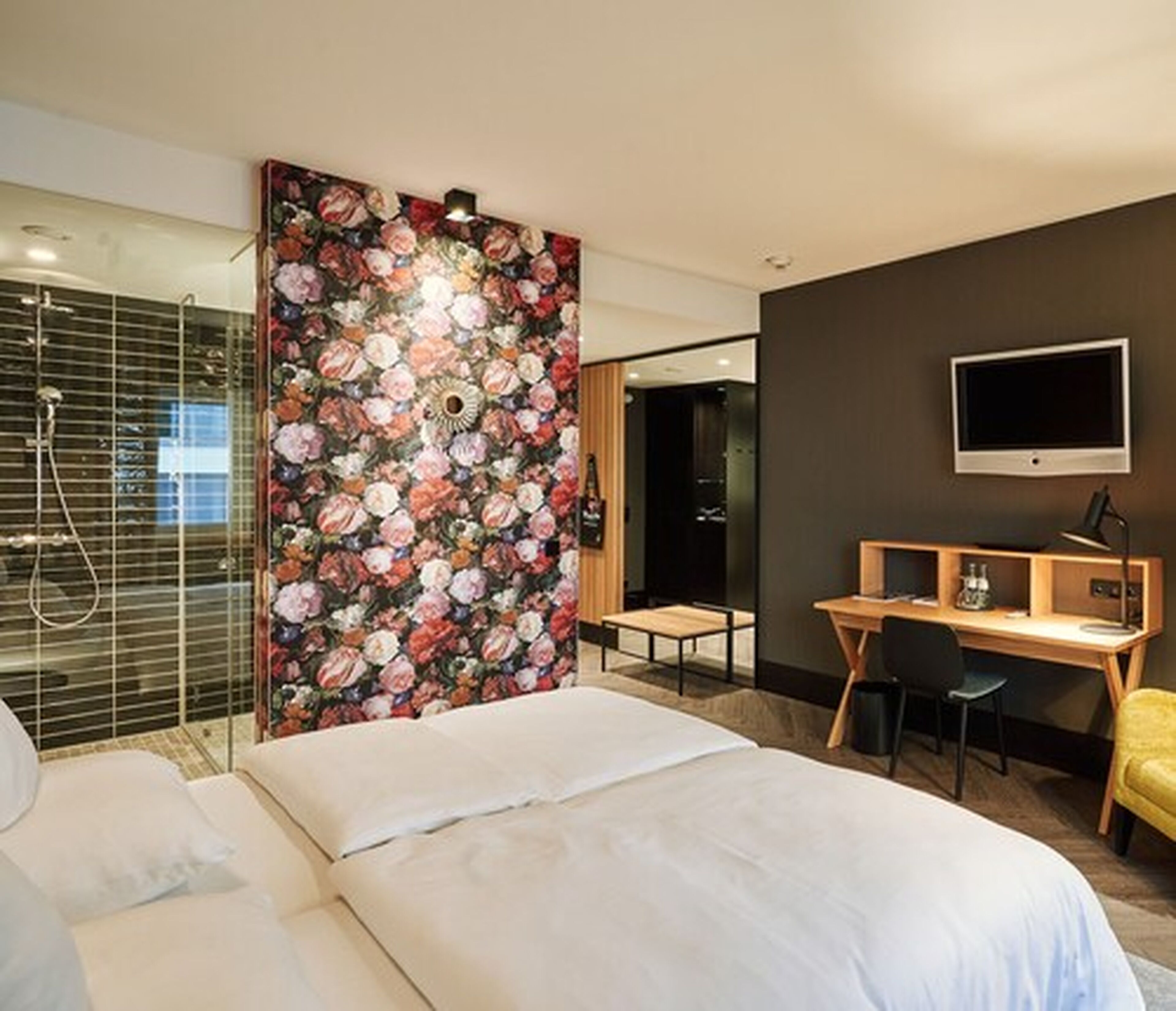 Ett modernt hotellrum med en stor säng, ett skrivbord, en stol, en TV och en duschhörna.