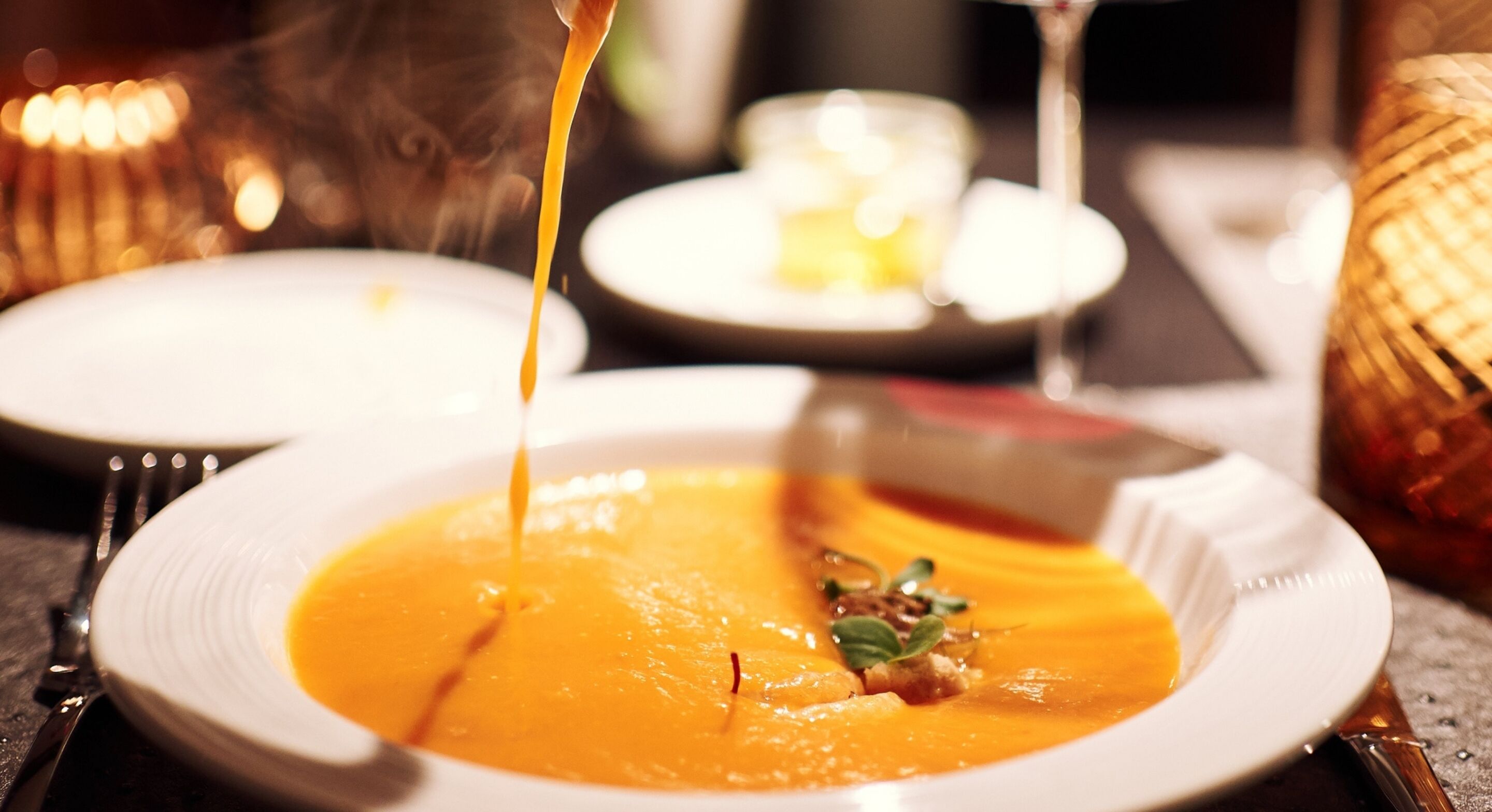Un tazón de sopa con adorno, un tenedor y un cuchillo sobre una mesa.