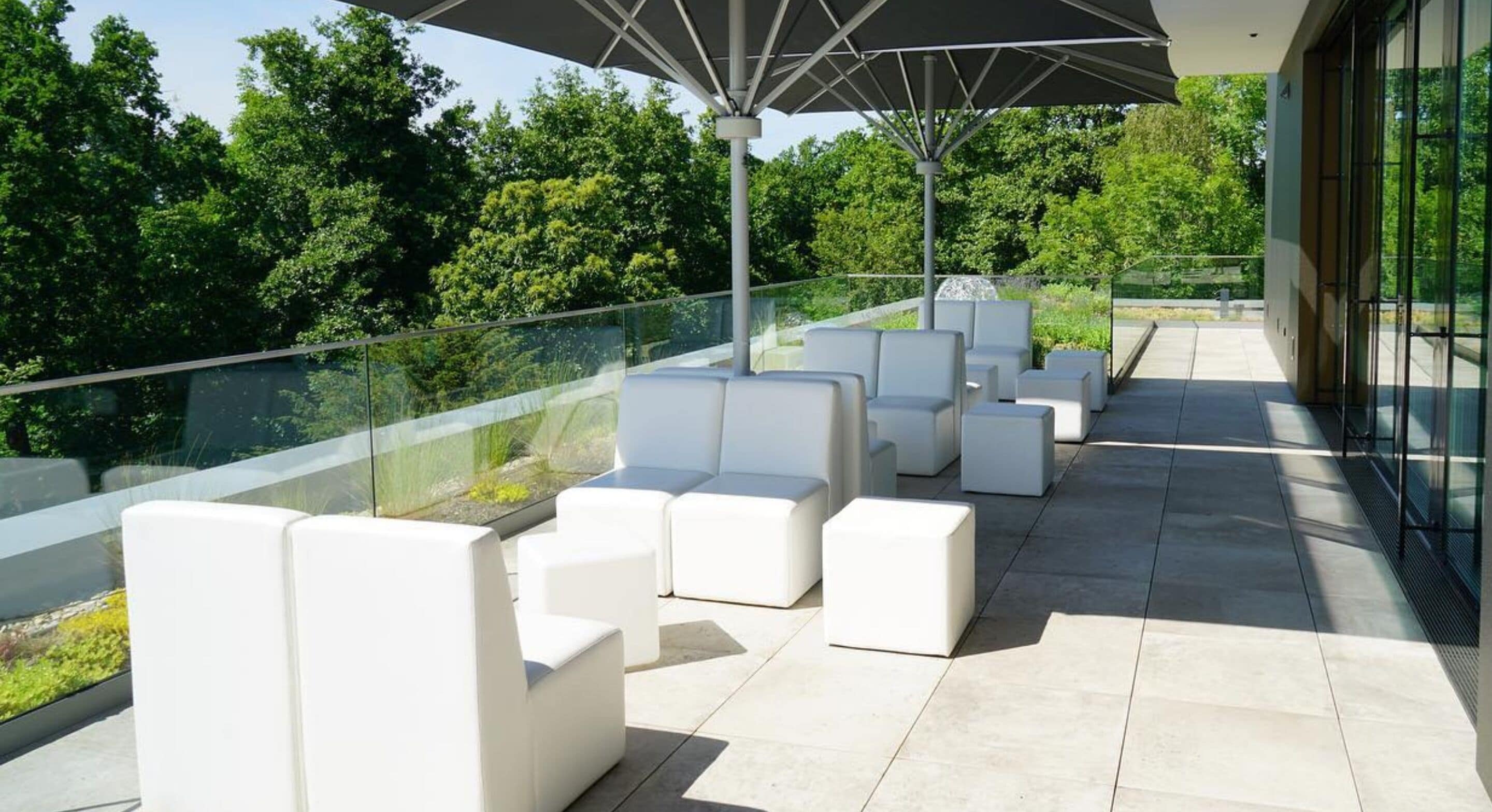 Een terras op het dak met witte modulaire zitplaatsen en een grote parasol.