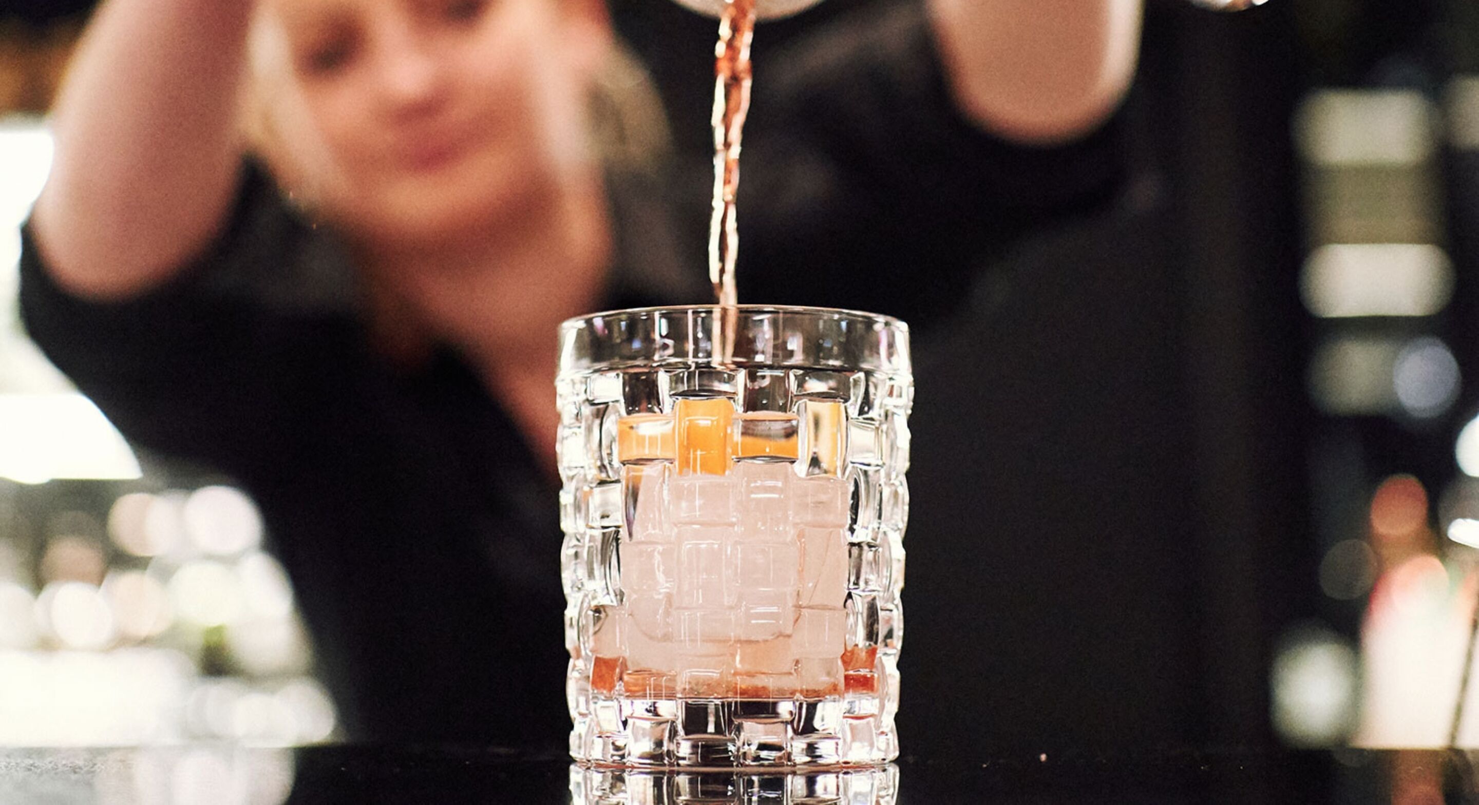 A bar setting with a clear glass containing a beverage being poured.
