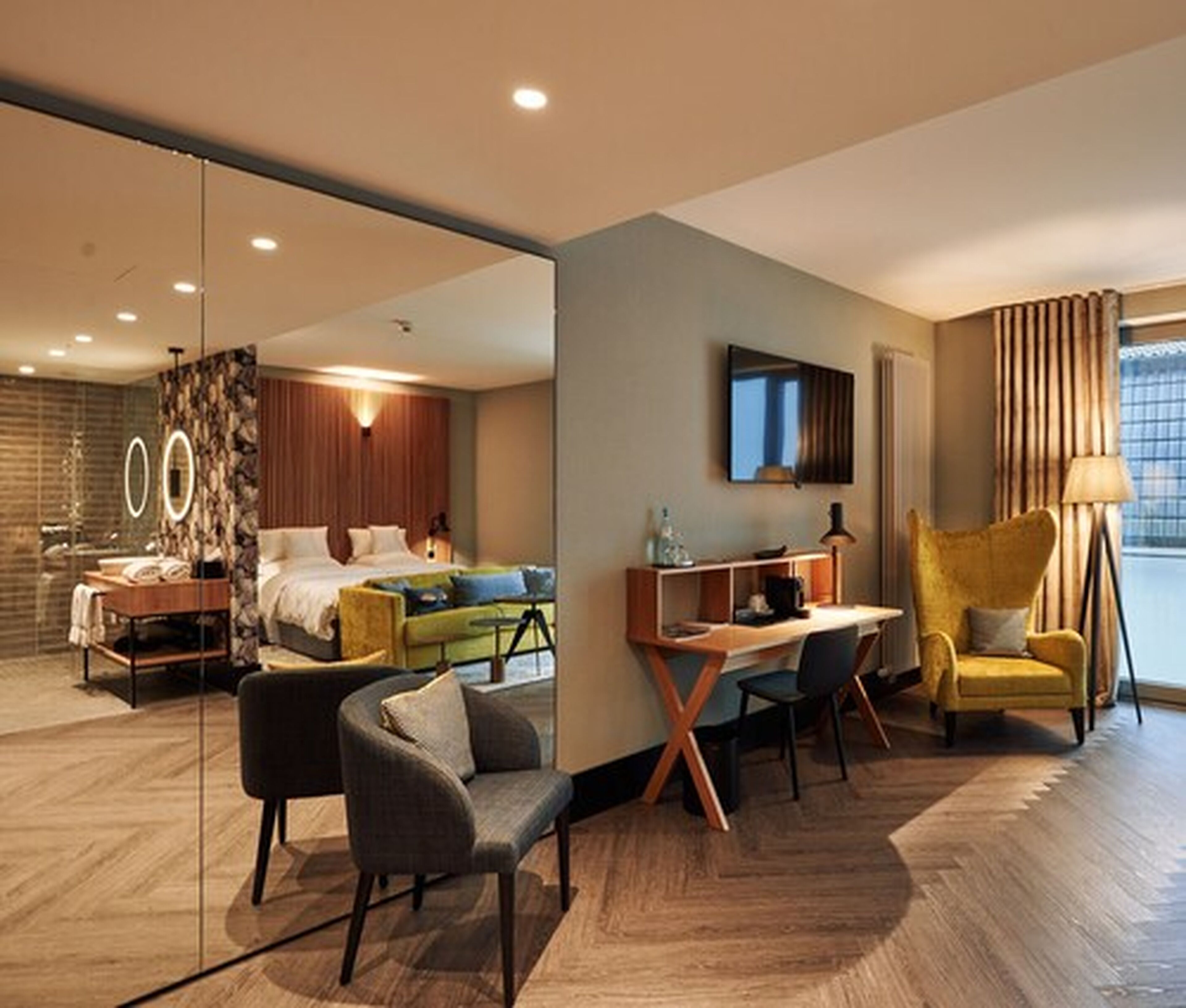 Una habitación de hotel moderna con una cama, un escritorio, una silla, un sofá y un espejo grande.