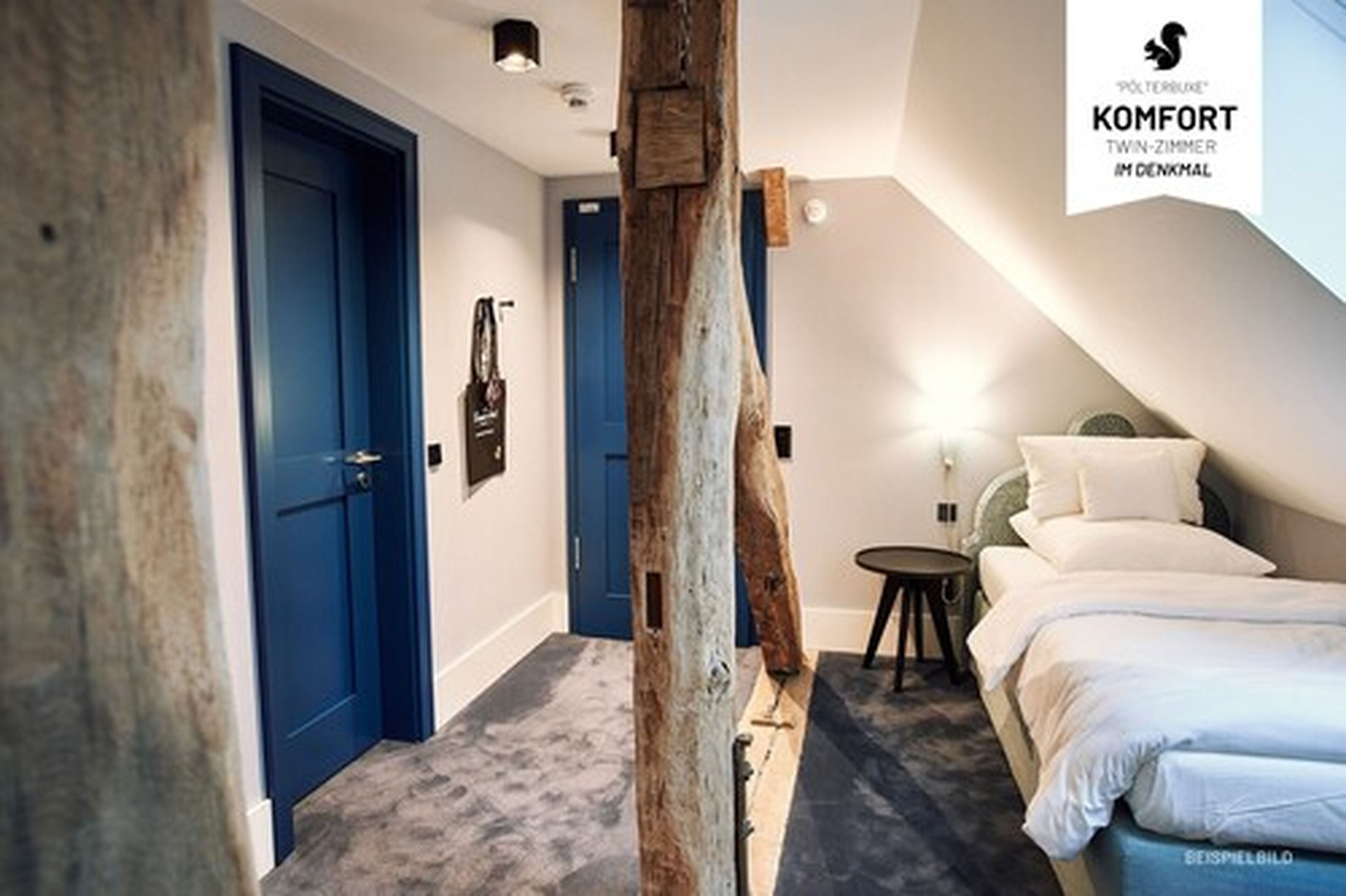A twin room with a wooden beam ceiling, a bed with white bedding, a small round table, and a blue door.