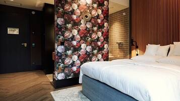 Ein modernes Hotelzimmer mit einem großen Bett, einer Wandverkleidung mit floralem Muster, einer Holzwand und einer kleinen Sitzecke mit einem Sessel.