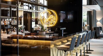Un área de bar moderna con un letrero de neón, una pantalla de televisión y una variedad de botellas y vasos en estantes.
