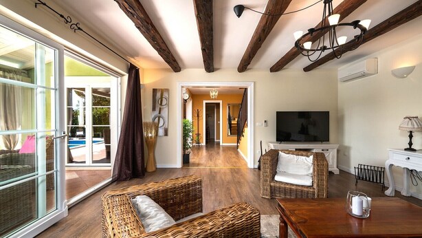 A spacious living room with a large sliding glass door leading to an outdoor area, a wooden ceiling, and a television on a white stand. - Spacious holiday house / pool / jacuzzi / playground / 6+2 (Rakalj)