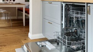 A modern kitchen with a built-in dishwasher, a wooden dining table with chairs, and a decorative wall panel. - Santa Croce Terrace - Luxury nest (Firenze)